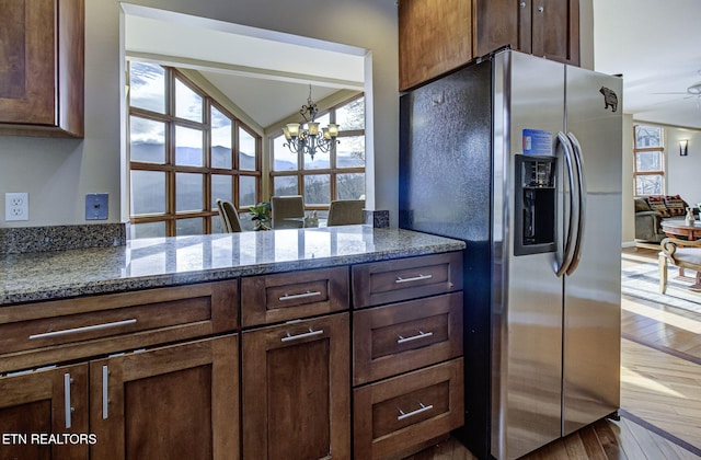 kitchen featuring stone counters, wood-type flooring, dark brown cabinetry, stainless steel fridge with ice dispenser, and ceiling fan with notable chandelier