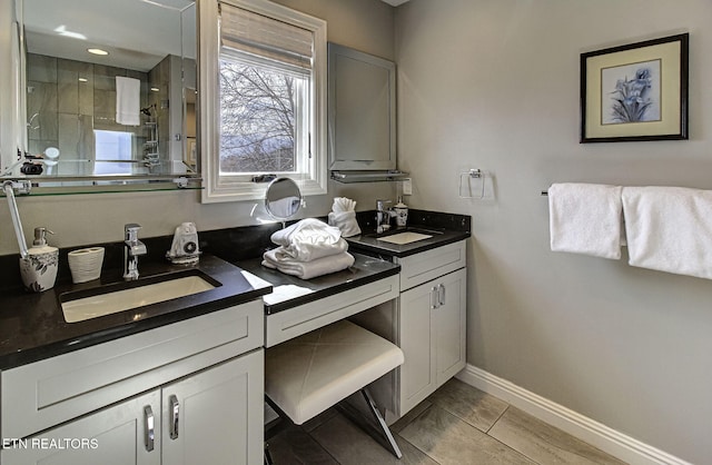 full bath with double vanity, baseboards, a tile shower, and a sink