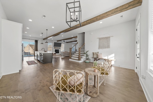 living room featuring stairs, beamed ceiling, wood finished floors, and a fireplace