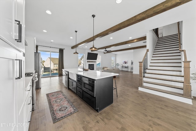 kitchen featuring a kitchen island with sink, a sink, open floor plan, dark cabinetry, and white cabinets