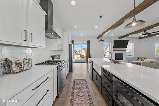 kitchen with white cabinetry, appliances with stainless steel finishes, open floor plan, and wall chimney range hood