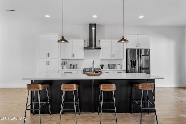 kitchen with a large island, white cabinets, stainless steel fridge, wall chimney exhaust hood, and tasteful backsplash