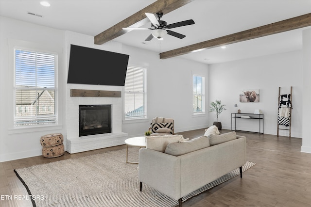 living area with visible vents, a brick fireplace, baseboards, beamed ceiling, and wood finished floors