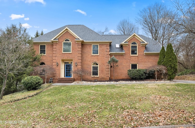 colonial inspired home with entry steps, a shingled roof, a front yard, and brick siding