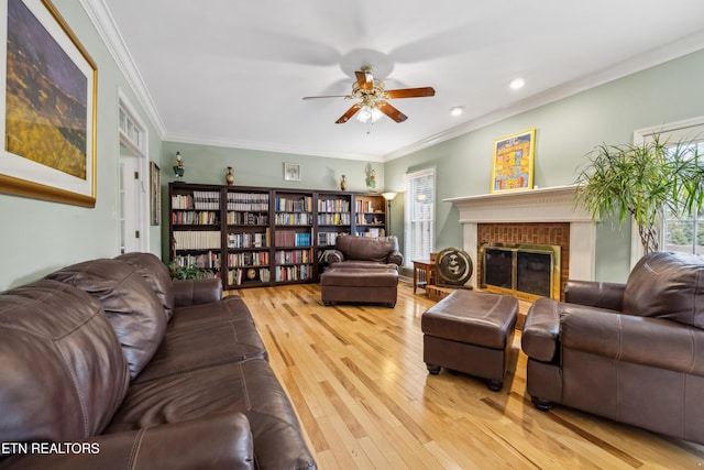 living area with ornamental molding, a fireplace, light wood-style flooring, and ceiling fan