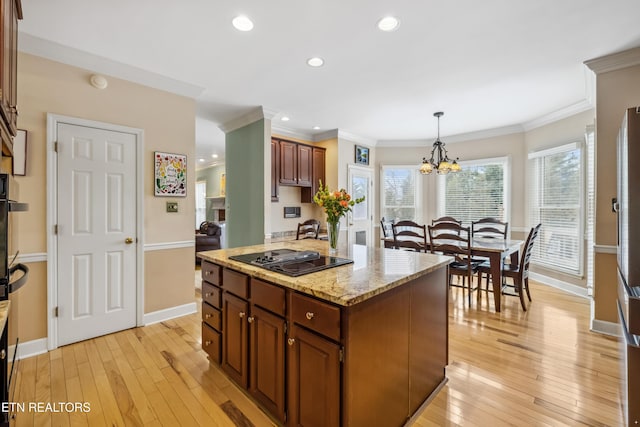 kitchen with baseboards, ornamental molding, light wood-type flooring, stovetop with downdraft, and decorative light fixtures