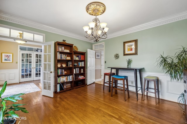 sitting room with french doors, a wainscoted wall, crown molding, a notable chandelier, and wood finished floors