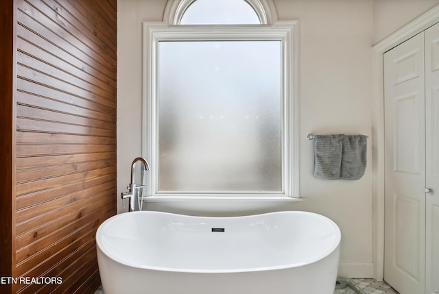 bathroom with marble finish floor and a soaking tub