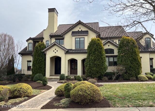 mediterranean / spanish-style home featuring a front lawn, a tiled roof, and a chimney