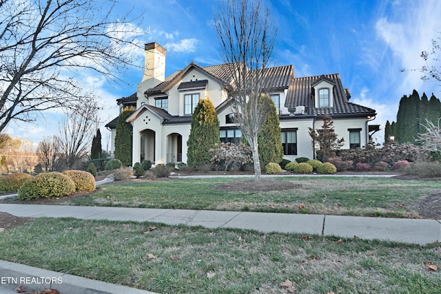 view of front of home with a tile roof, stucco siding, a front lawn, and a chimney