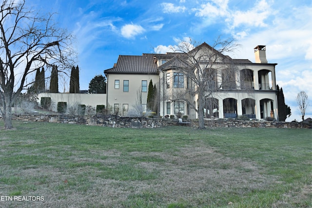 view of front of home featuring a balcony, a chimney, a front lawn, and metal roof