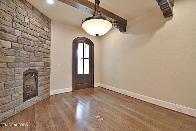 entryway featuring wood finished floors, baseboards, arched walkways, a stone fireplace, and beamed ceiling