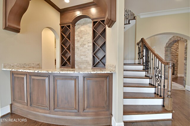 wine area with baseboards, wood finished floors, arched walkways, and ornamental molding