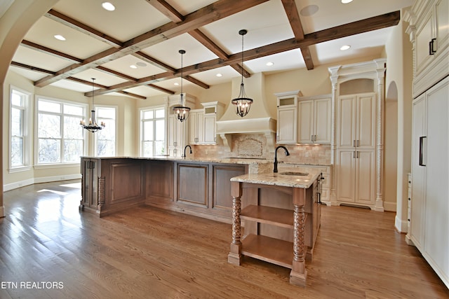 kitchen with a sink, backsplash, light wood-type flooring, arched walkways, and a kitchen island with sink