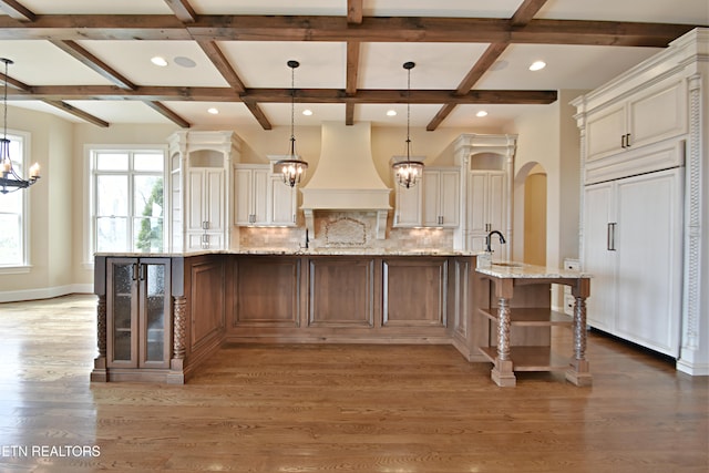 kitchen with paneled fridge, premium range hood, arched walkways, decorative backsplash, and a chandelier