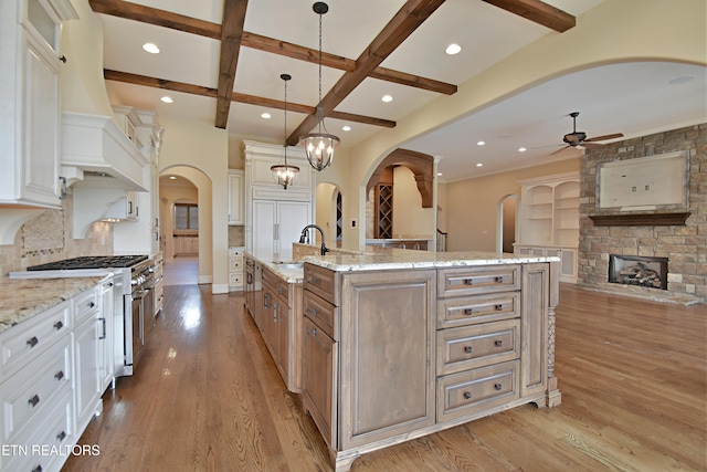 kitchen with beam ceiling, a ceiling fan, arched walkways, stainless steel stove, and light wood finished floors