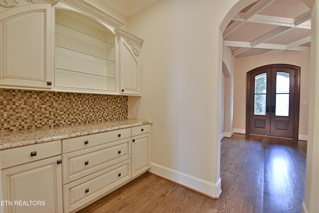 interior space featuring decorative backsplash, cream cabinetry, arched walkways, and coffered ceiling