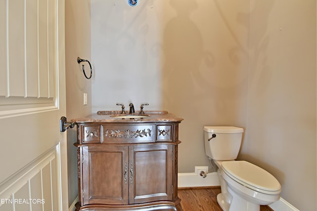 bathroom featuring baseboards, toilet, wood finished floors, and vanity