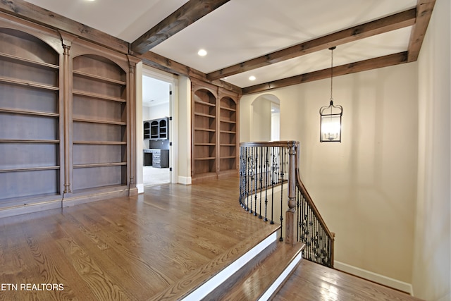 corridor featuring baseboards, an upstairs landing, arched walkways, and wood finished floors