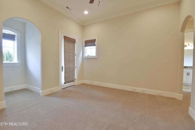 spare room featuring plenty of natural light, arched walkways, visible vents, and light carpet