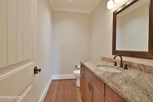 bathroom featuring vanity, wood finished floors, baseboards, crown molding, and toilet