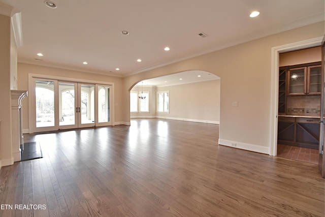 unfurnished living room featuring wood finished floors, baseboards, recessed lighting, arched walkways, and crown molding