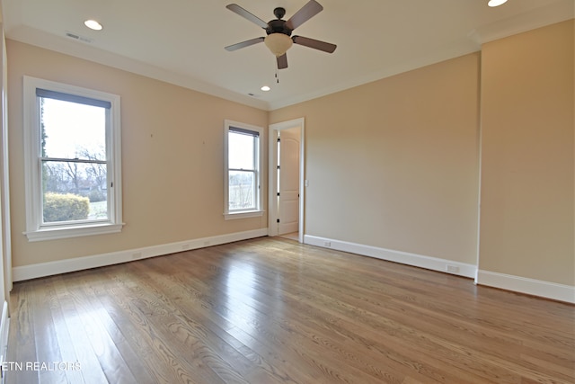 empty room featuring visible vents, baseboards, ornamental molding, and light wood finished floors