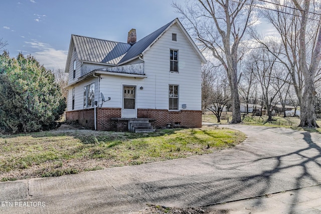 view of property exterior with brick siding, metal roof, and a chimney