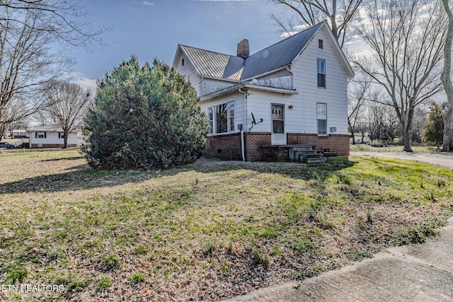 view of side of home featuring a yard, brick siding, metal roof, and a chimney