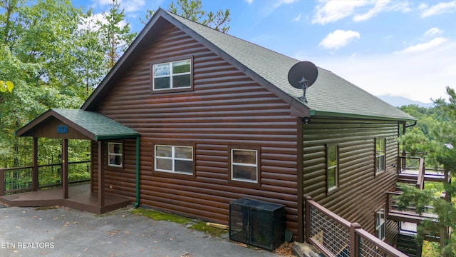 view of home's exterior with roof with shingles, log veneer siding, and a wooden deck