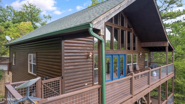 view of home's exterior with a shingled roof, faux log siding, and french doors