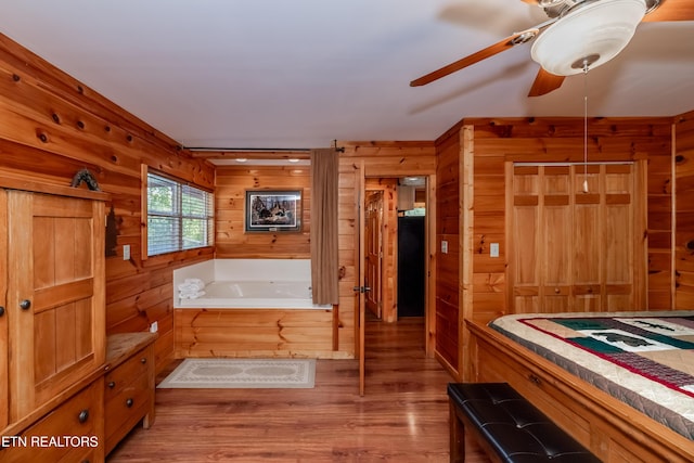 bathroom with ceiling fan, wood finished floors, a bath, and wooden walls