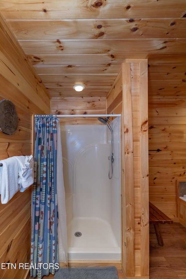 full bath featuring wood ceiling, wooden walls, a shower stall, and wood finished floors