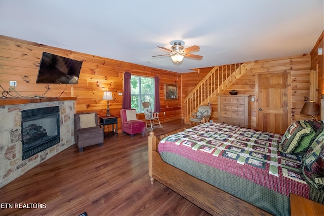 bedroom featuring wood walls, a fireplace, a ceiling fan, and wood finished floors