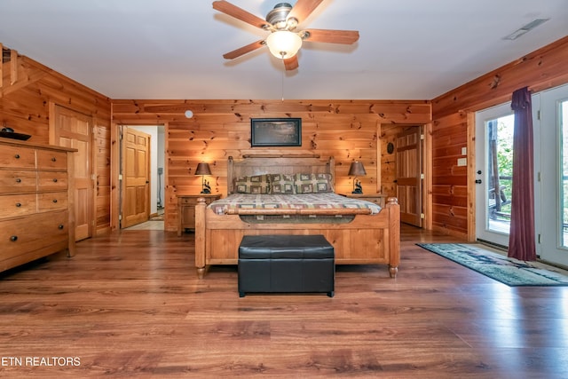 bedroom with access to outside, wooden walls, visible vents, and wood finished floors