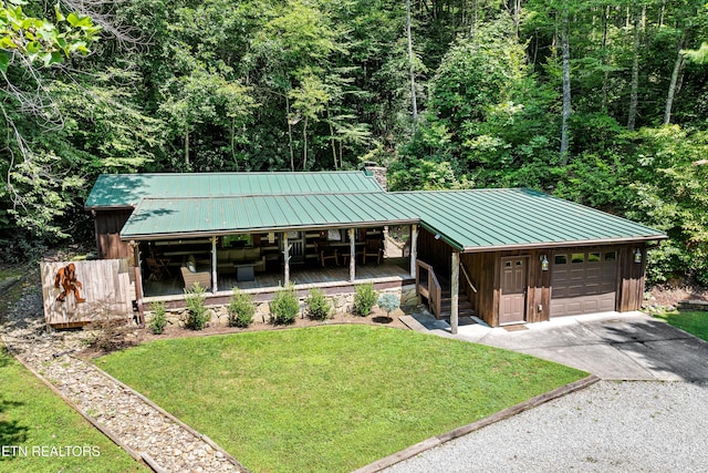 chalet / cabin featuring a porch, concrete driveway, board and batten siding, a standing seam roof, and a front lawn