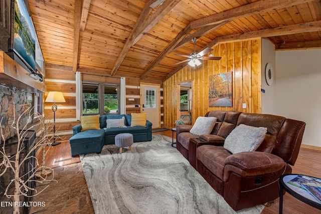 living area featuring lofted ceiling with beams, wooden ceiling, wood finished floors, a stone fireplace, and wood walls