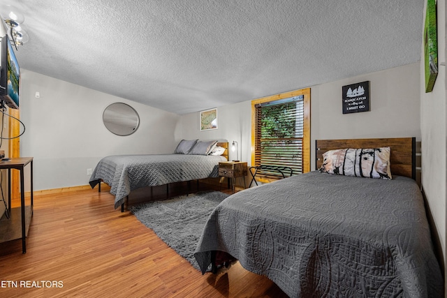 bedroom with a textured ceiling, wood finished floors, and baseboards