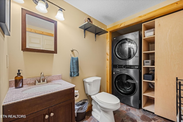 bathroom featuring stacked washer and dryer, toilet, stone finish floor, a textured ceiling, and vanity