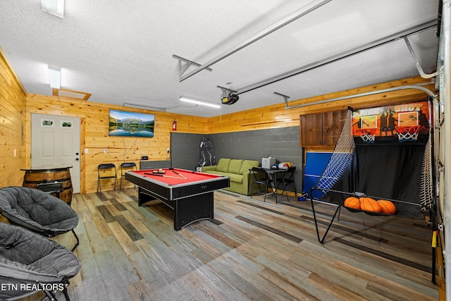 rec room with a garage, concrete block wall, billiards, wooden walls, and wood finished floors