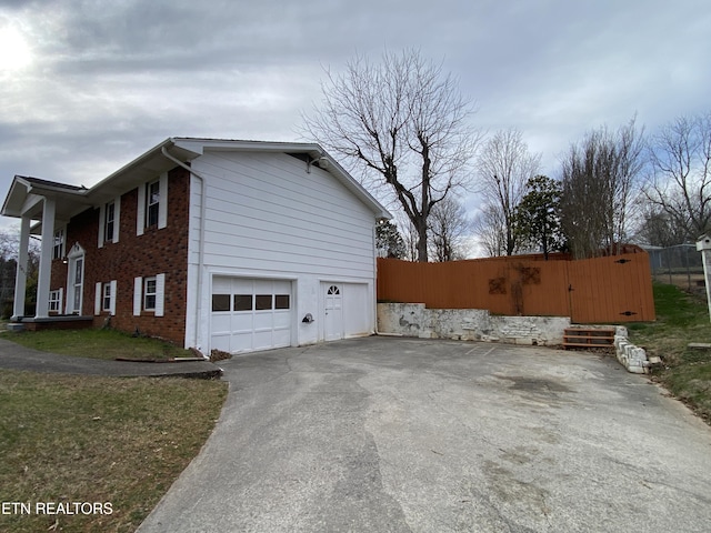 view of home's exterior with driveway, brick siding, an attached garage, and fence