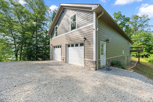 view of home's exterior featuring a garage, stone siding, and gravel driveway