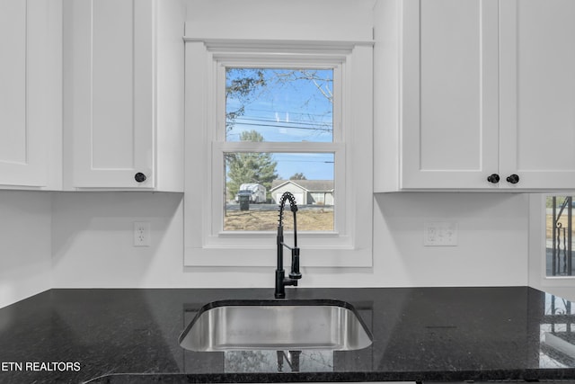 kitchen featuring dark stone counters, a sink, and white cabinets