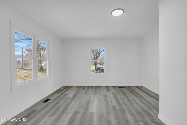 empty room featuring baseboards, visible vents, a wealth of natural light, and wood finished floors