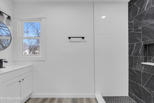 bathroom featuring tiled shower, vanity, baseboards, and wood finished floors