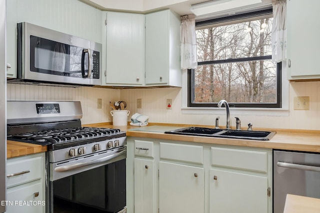 kitchen featuring stainless steel appliances, butcher block countertops, a sink, and white cabinetry