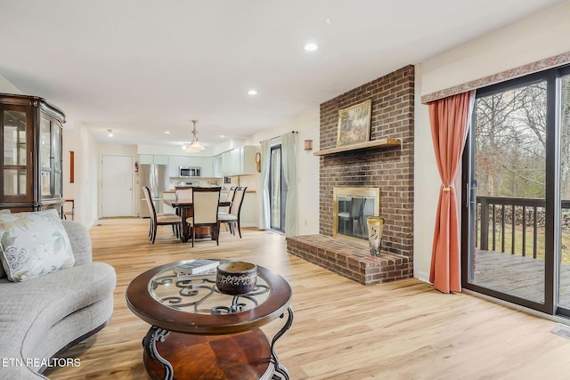 living area with light wood finished floors, a brick fireplace, visible vents, and recessed lighting