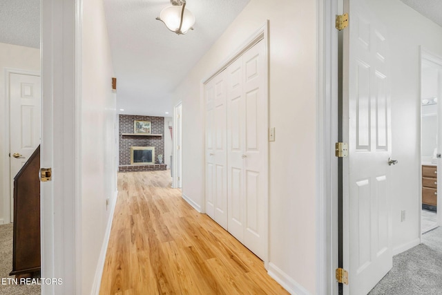 corridor featuring a textured ceiling, light wood-style floors, and baseboards