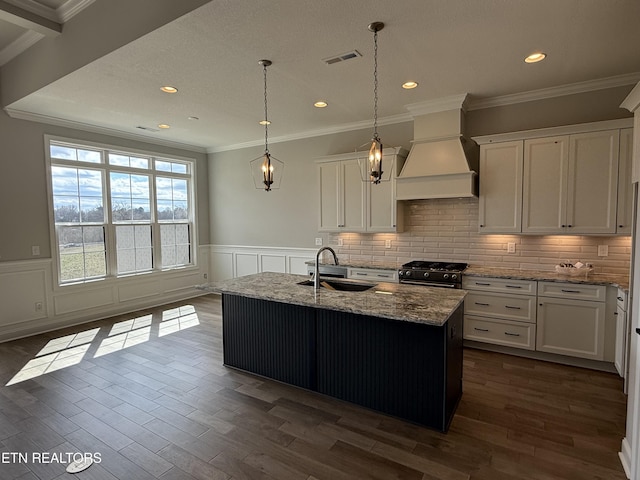 kitchen with custom exhaust hood, visible vents, gas stove, white cabinetry, and a sink