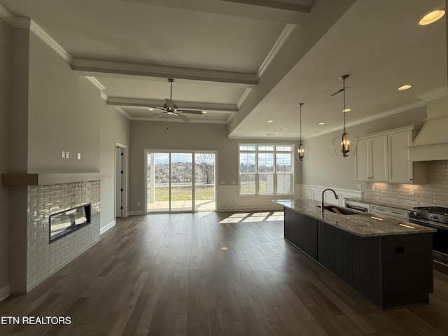 kitchen featuring a wainscoted wall, a sink, open floor plan, light stone countertops, and gas range